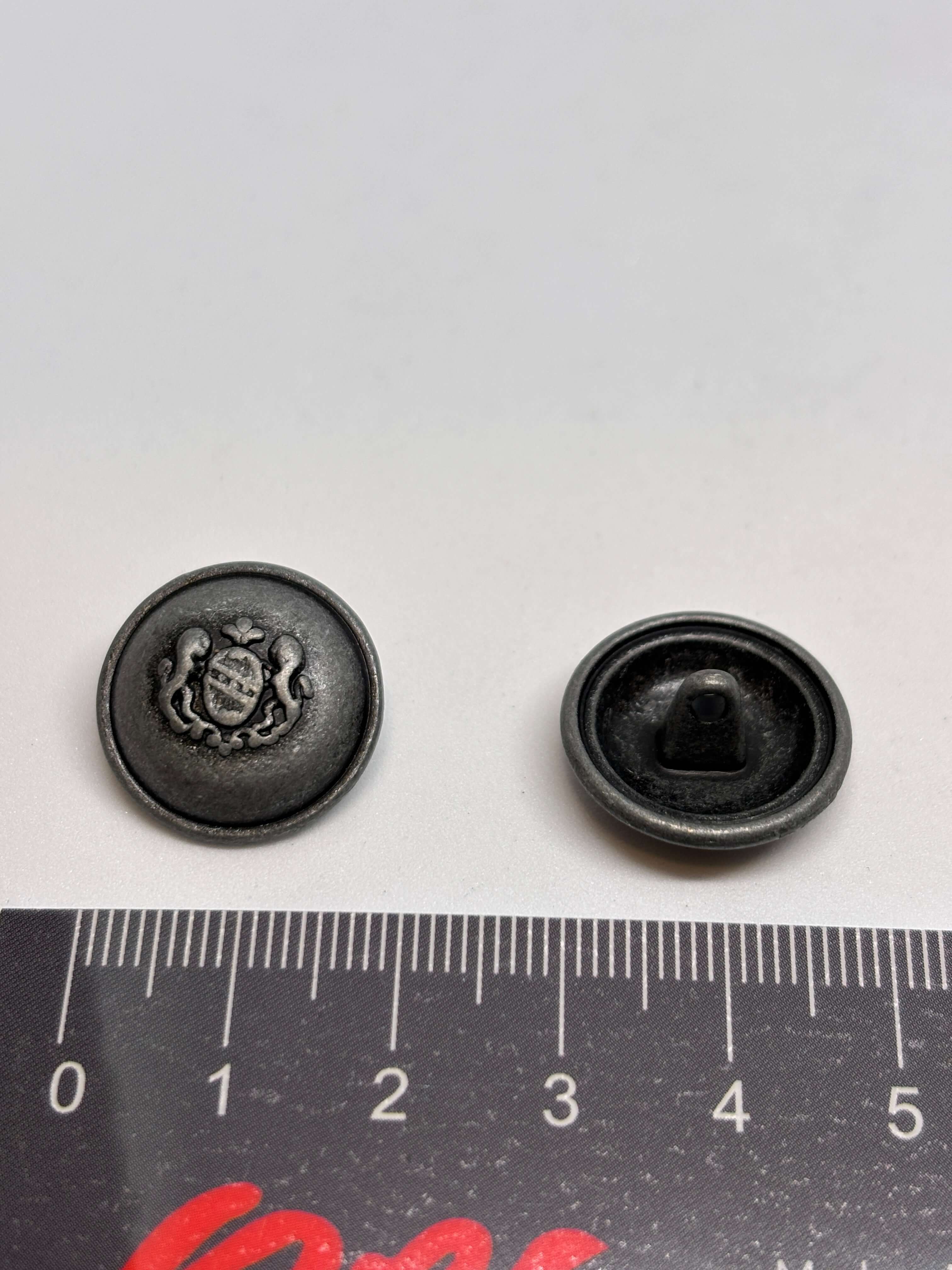 Botón 54549 de vástago en plata antigua con diseño de cresta heráldica, ideal para prendas medianas. button