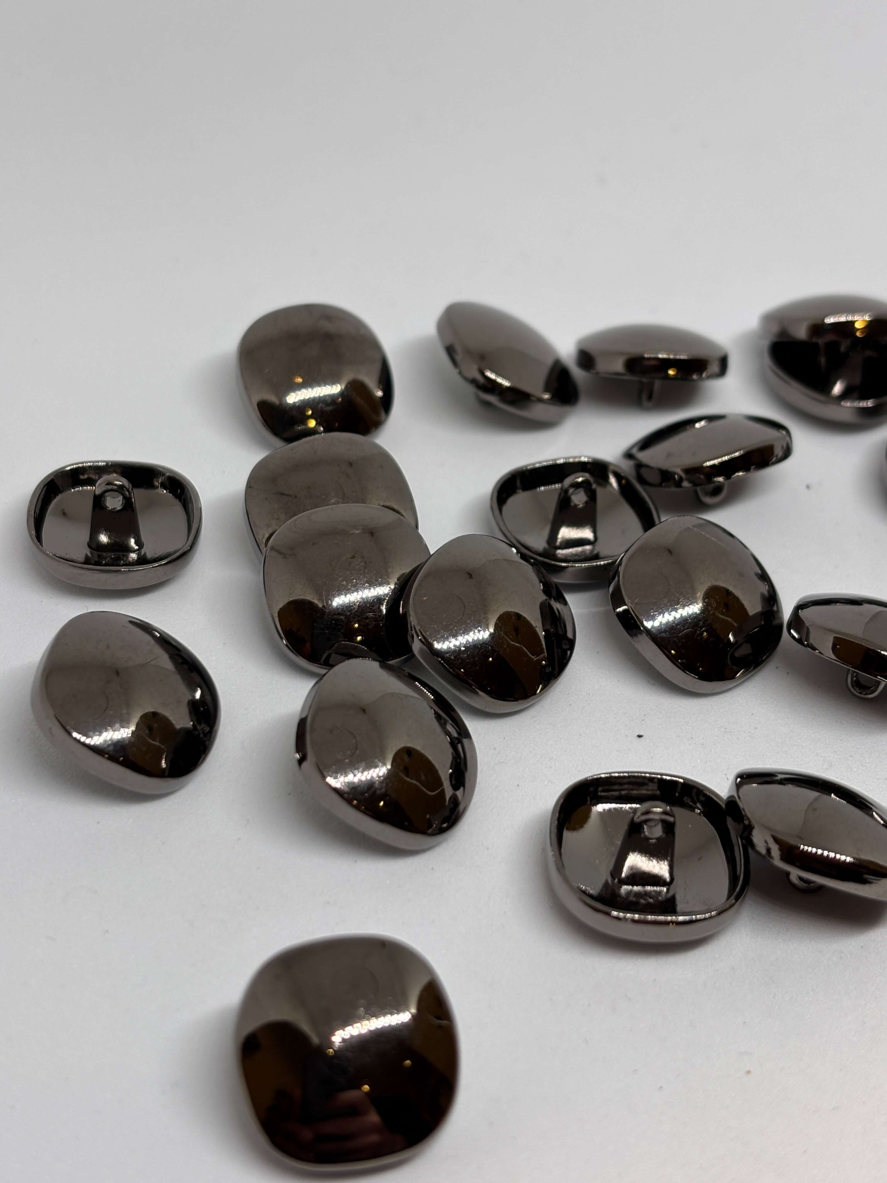 Botón Piedra de forma ovalada con acabado brillante y color gris oscuro sobre fondo claro. button