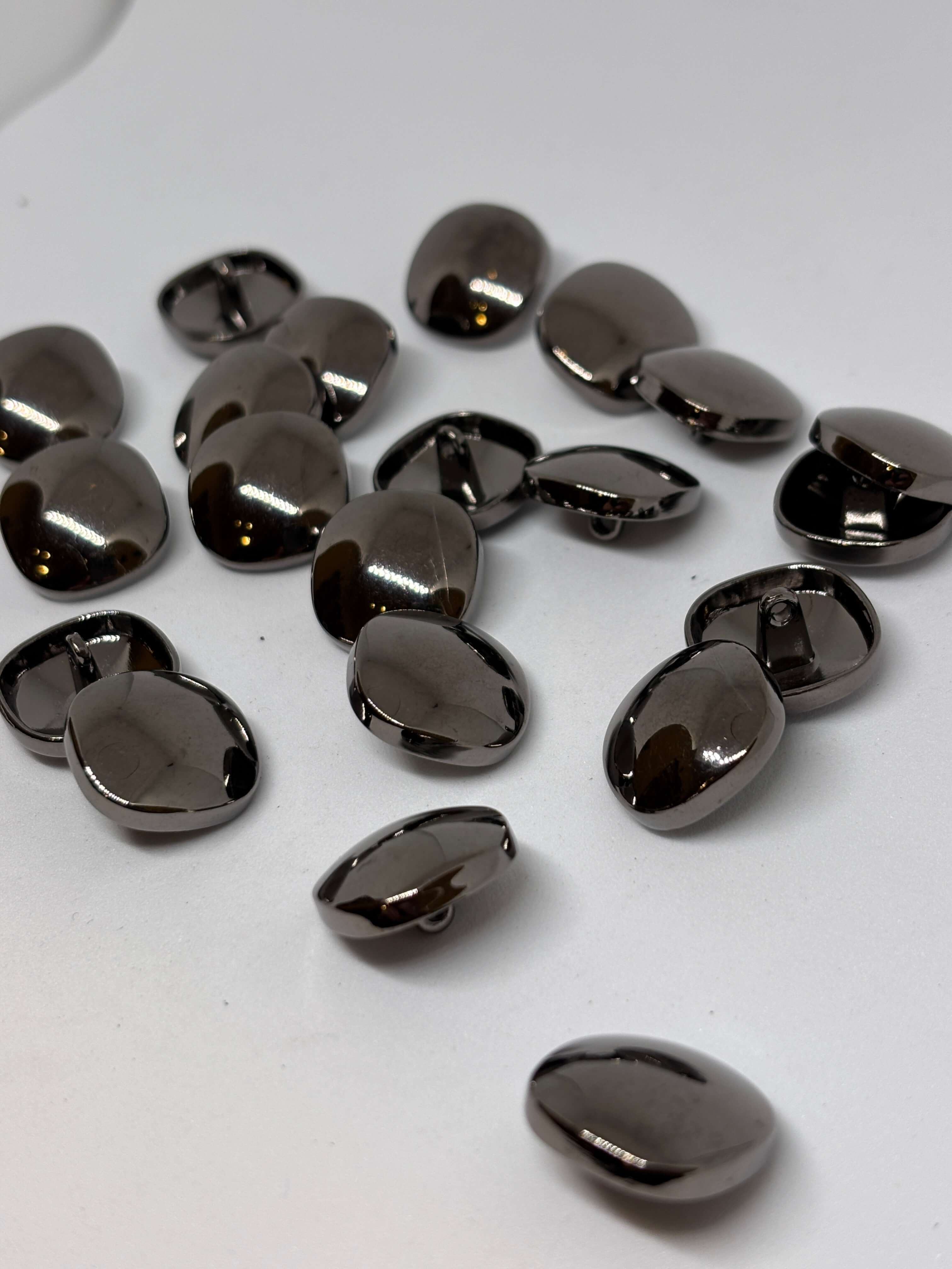 Botón Piedra de forma ovalada con acabado brillante y color gris oscuro sobre fondo claro. button