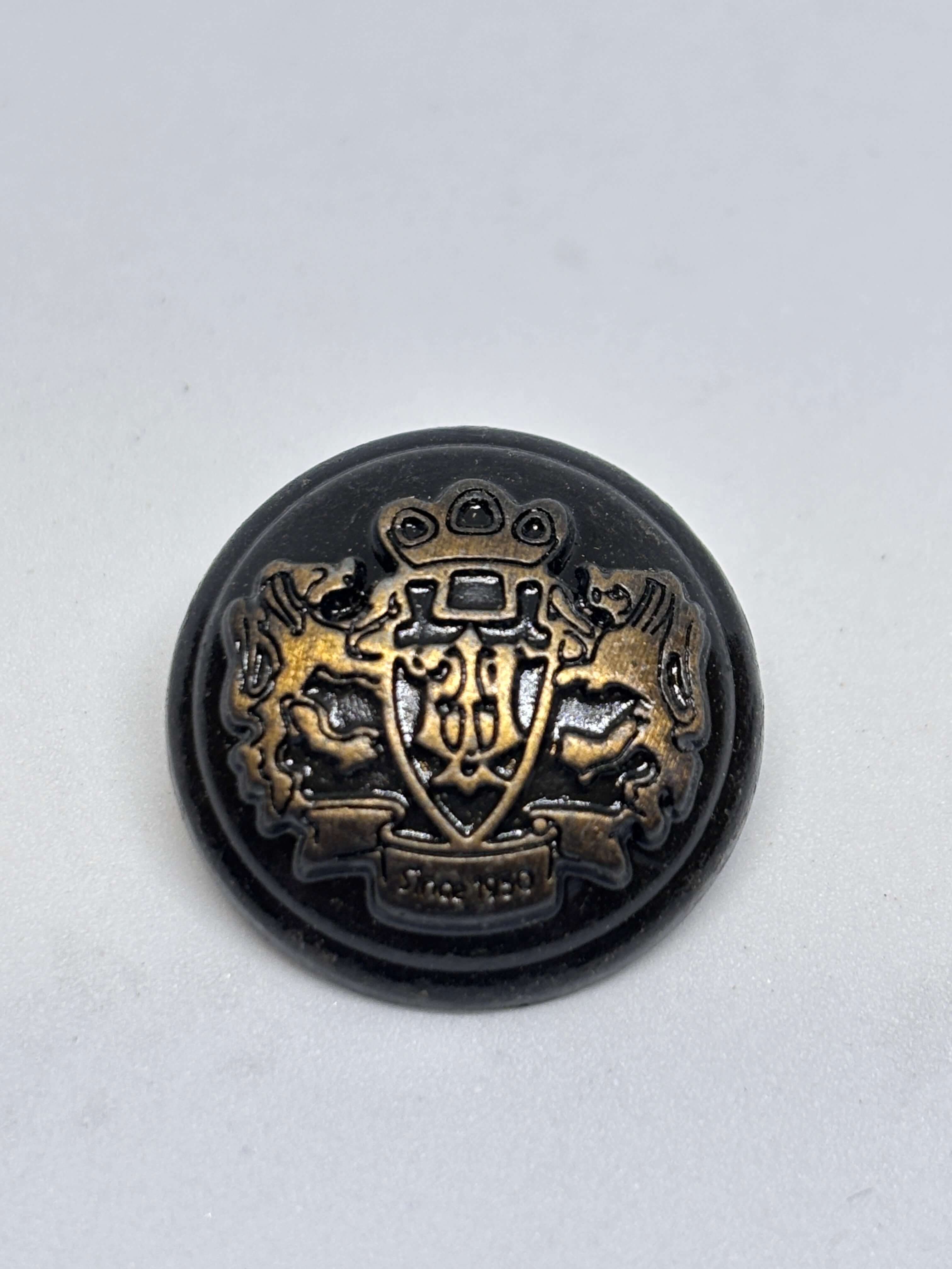 Botón M55300 de vástago en bronce antiguo con cresta heráldica y detalle en relieve, disponible en talla 20-22mm. button
