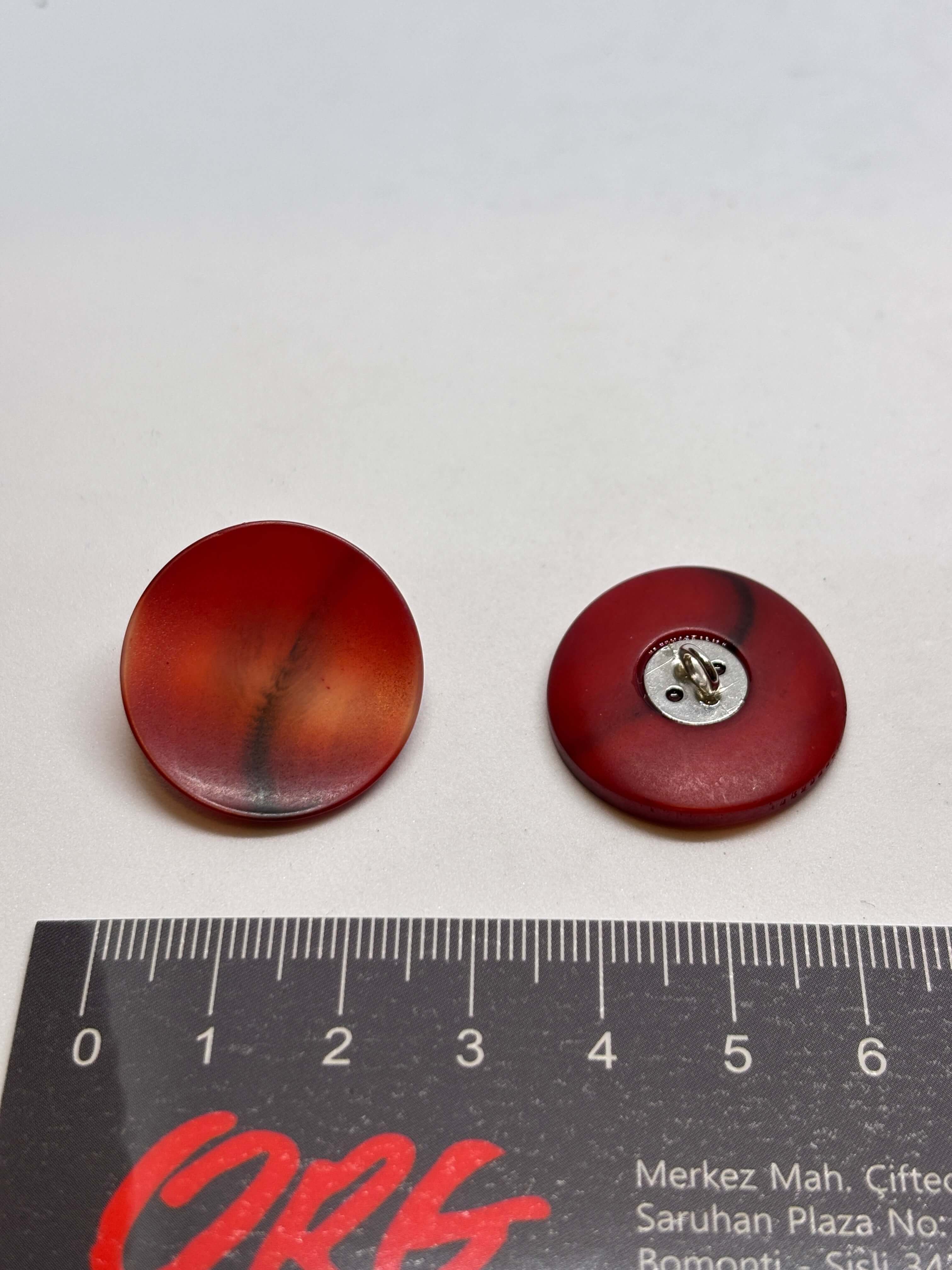 Botón redondo de color rojo, material plástico, con acabado brillante y diseño suave, ideal para prendas de vestir. button