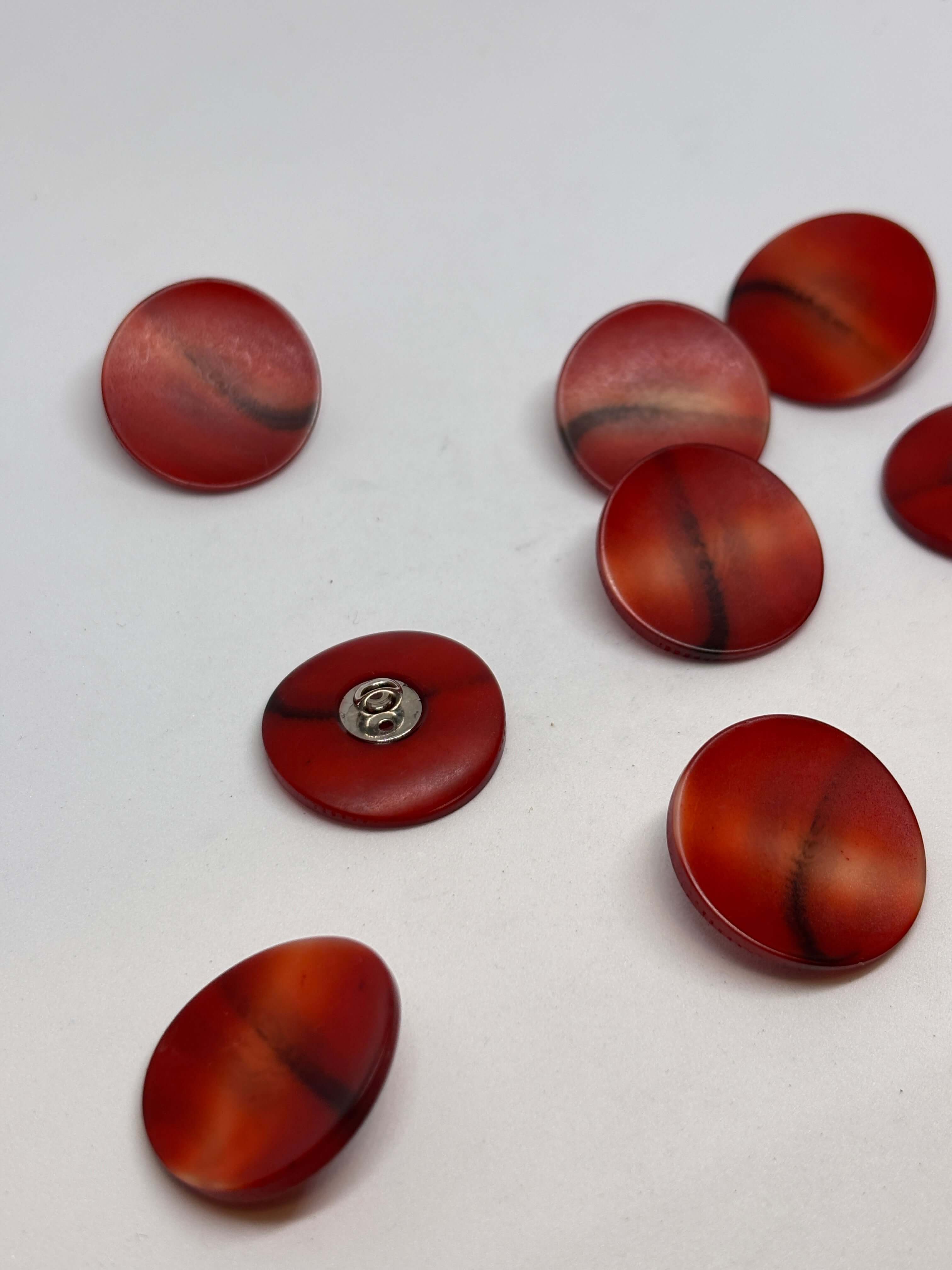 Botón redondo de color rojo, material plástico, con acabado brillante y diseño suave, ideal para prendas de vestir. button