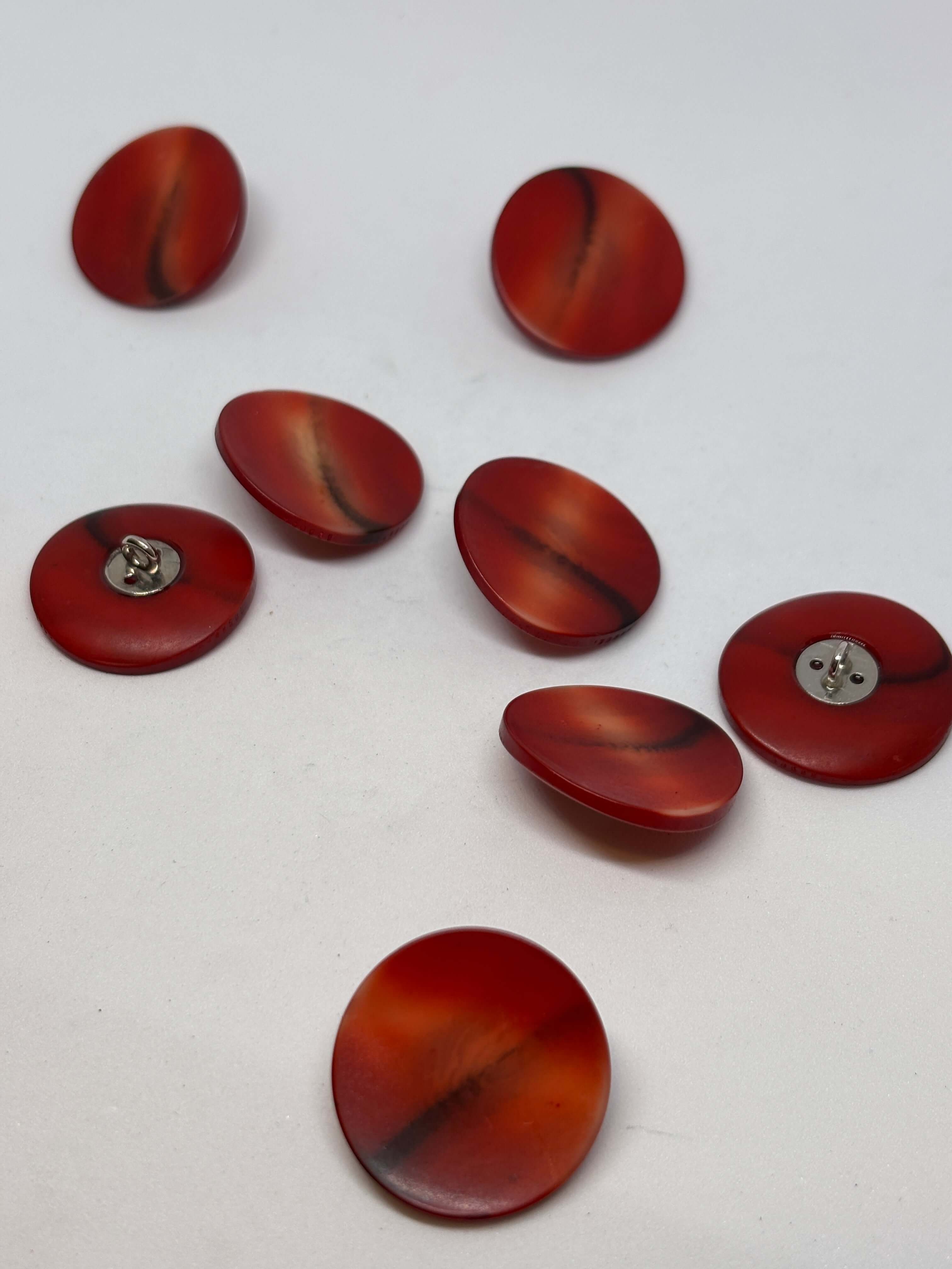 Botón redondo de color rojo, material plástico, con acabado brillante y diseño suave, ideal para prendas de vestir. button