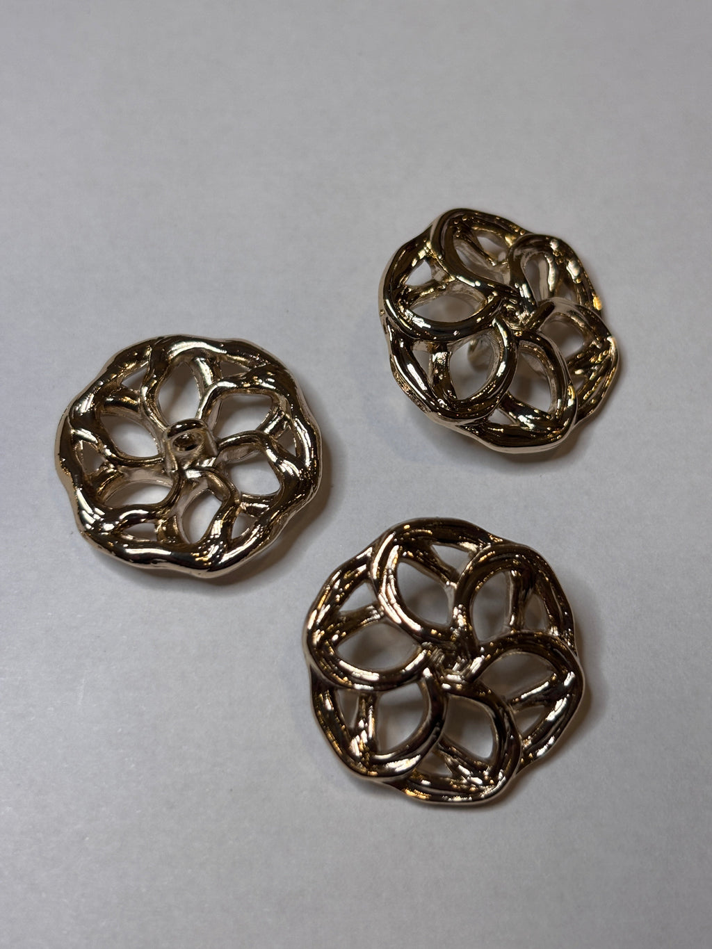 Three decorative metal buttons in a floral design, showcasing their intricate detailing and shine. boton