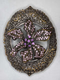 Belt buckle with ornate floral design and pink gemstones, showcasing a decorative vintage style. Hebilla de cinturon