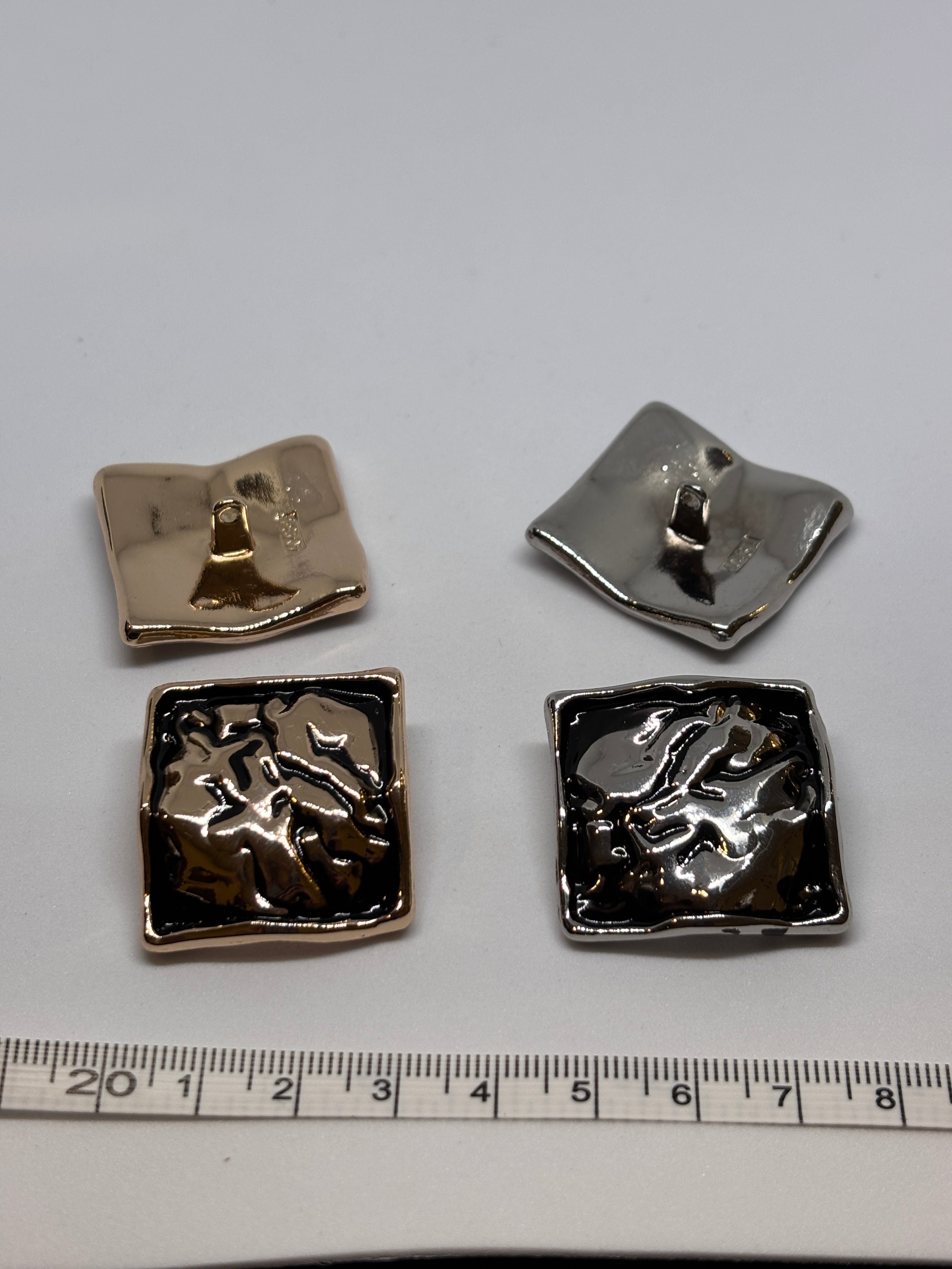 Shiny metal buttons in a square shape, showcasing a 32mm (50") shank button design. boton